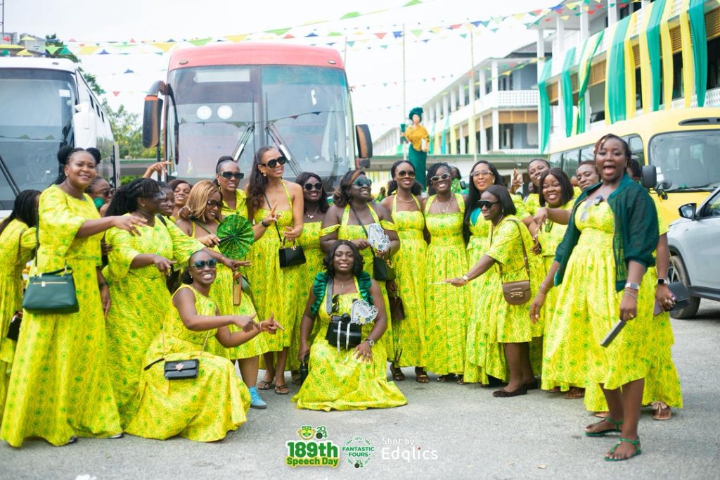 Large group in matching yellow and green dresses in front of buses, 189th Speech Day