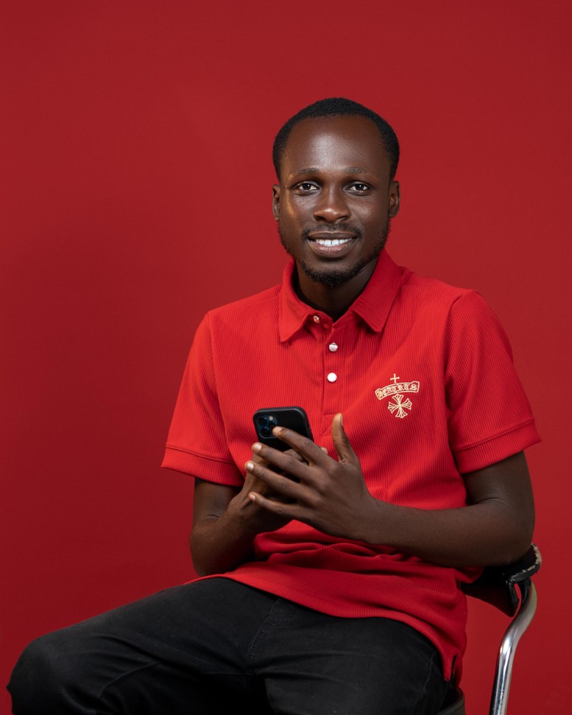 Studio portrait in red polo against red backdrop, holding a smartphone